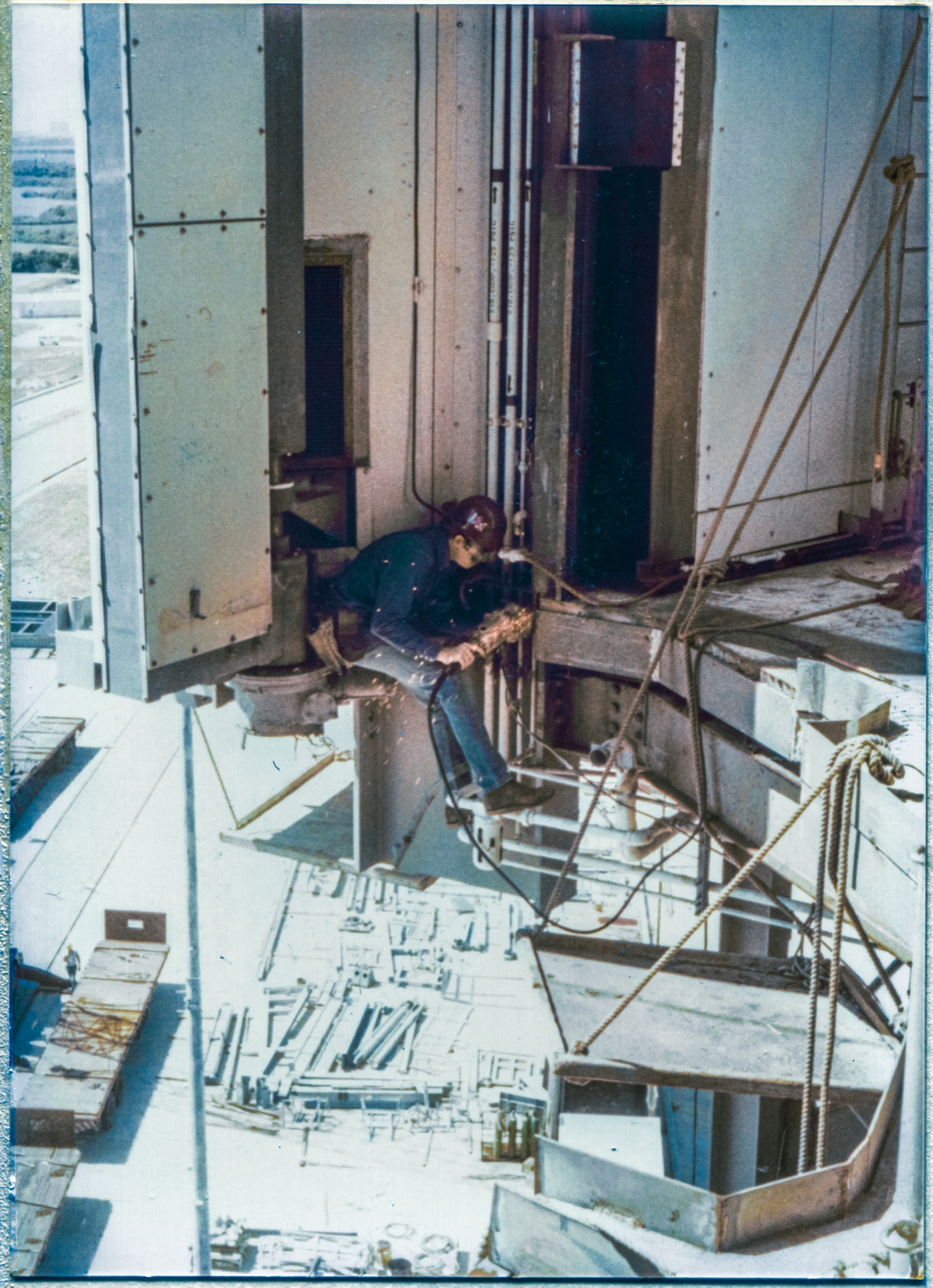 Image 059. Union Ironworker. Local 808. Working for Ivey's Steel Erectors on the Rotating Service Structure at Space Shuttle Launch Complex 39-B, Kennedy Space Center, Florida. I do not recall this man’s name, alas. No harness. This the way we did the work, back in the early 1980’s, and nobody minded, and nobody ever fell, and nobody ever even got sensibly hurt. He is grinding a weld smooth, which he just laid in to the new framing steel at elevation 135’-7” which is the Main Floor level of the Payload Changeout Room, and which abuts the top edge of the orbiter’s OMS Pods when the RSS is mated to it, and which was extensively modified to accommodate the installation of the OMS Pod Heated Purge Covers, which turned out to be a spectacularly-bad idea, both conceptually and physically. We did not like the OMS Pod Heated Purge Covers, and those ironworkers who were the most savvy regarding the ways of things like this disliked them the most. They knew what was coming. And they told those of us in the field trailers, and we told NASA, and NASA handed it to their best engineers to give it their regarded consideration… and then told us to proceed with the Covers, anyway. And just as those most-savvy ironworkers said it would, it did not end well. Photo by James MacLaren. Image 059. Union Ironworker. Local 808. Working for Ivey's Steel Erectors on the Rotating Service Structure at Space Shuttle Launch Complex 39-B, Kennedy Space Center, Florida. I do not recall this man’s name, alas. No harness. This the way we did the work, back in the early 1980’s, and nobody minded, and nobody ever fell, and nobody ever even got sensibly hurt. He is grinding a weld smooth, which he just laid in to the new framing steel at elevation 135’-7” which is the Main Floor level of the Payload Changeout Room, and which abuts the top edge of the orbiter’s OMS Pods when the RSS is mated to it, and which was extensively modified to accommodate the installation of the OMS Pod Heated Purge Covers, which turned out to be a spectacularly-bad idea, both conceptually and physically. We did not like the OMS Pod Heated Purge Covers, and those ironworkers who were the most savvy regarding the ways of things like this disliked them the most. They knew what was coming. And they told those of us in the field trailers, and we told NASA, and NASA handed it to their best engineers to give it their regarded consideration… and then told us to proceed with the Covers, anyway. And just as those most-savvy ironworkers said it would, it did not end well. Photo by James MacLaren.